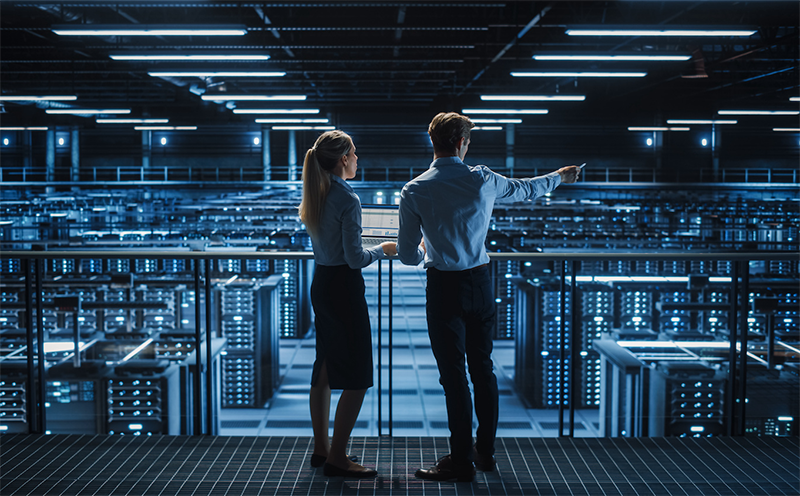 A imagem mostra um homem e uma mulher no corredor de datacenters on-premise.