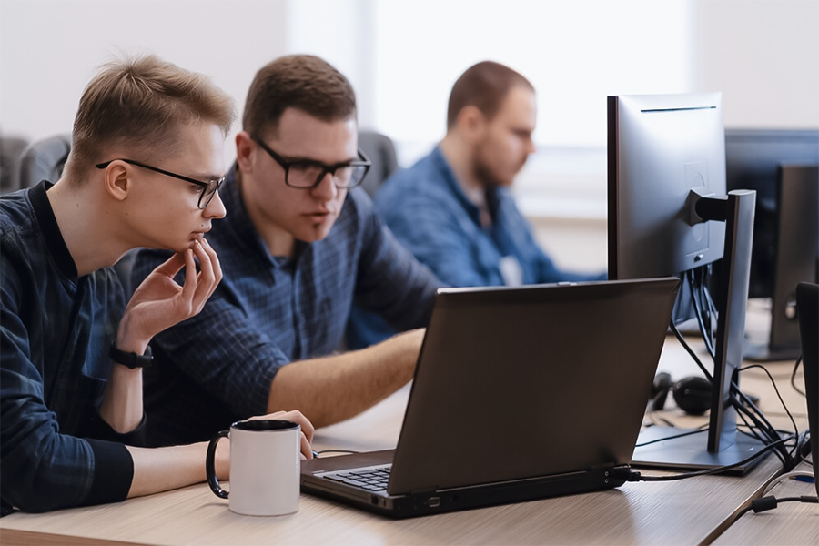 três homens em reunião sobre ti olhando para computador